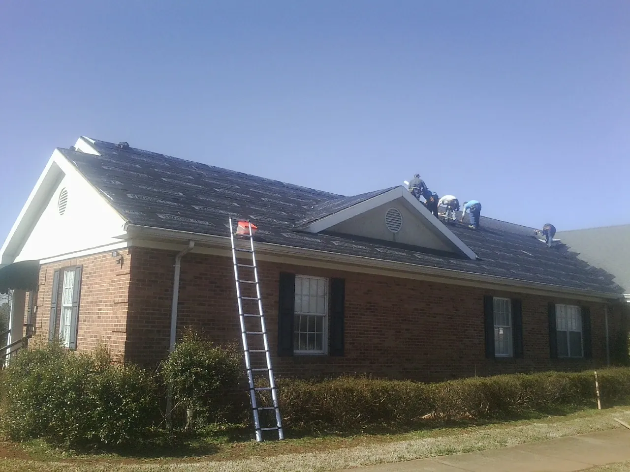 Crew tearing shingles off a brick ranch roof with a ladder set — Metal Roof Repair work by our crew in Feura Bush