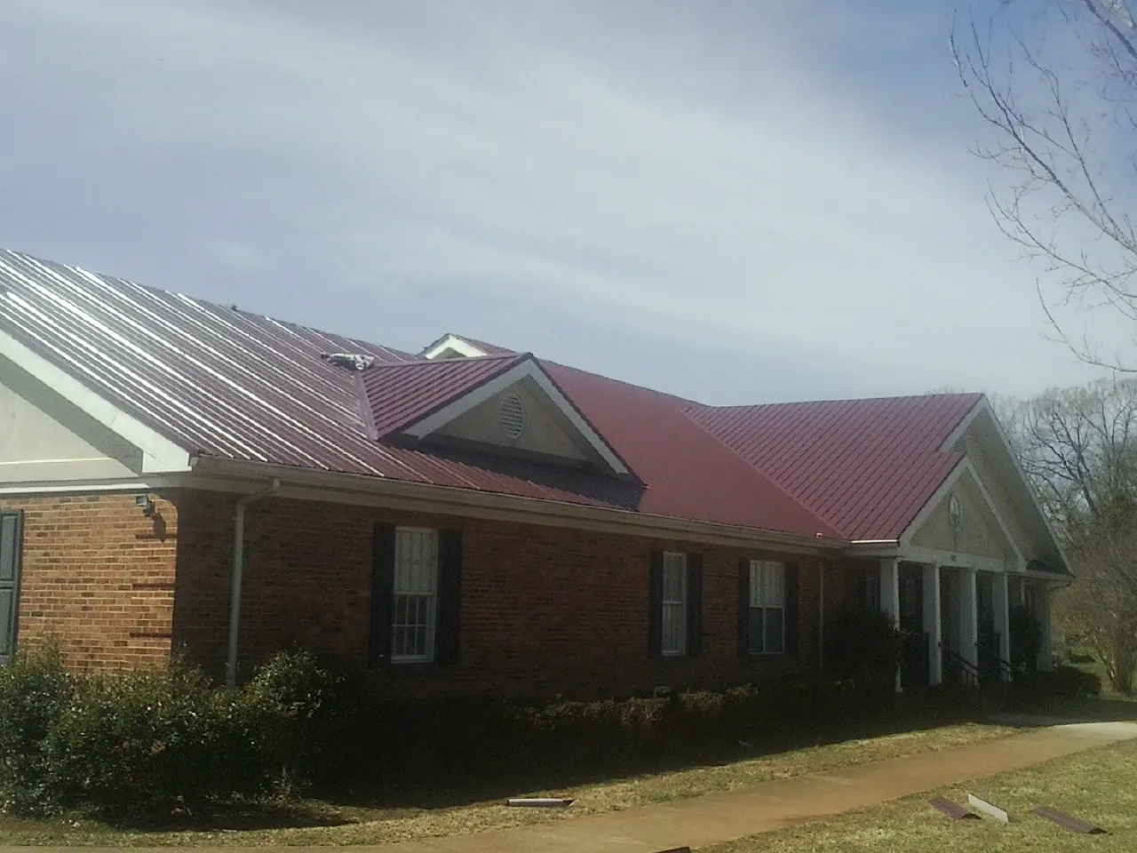 Red metal roof with gabled entries on a long brick building, from a Hail Damage Roof Repair job in Feura Bush