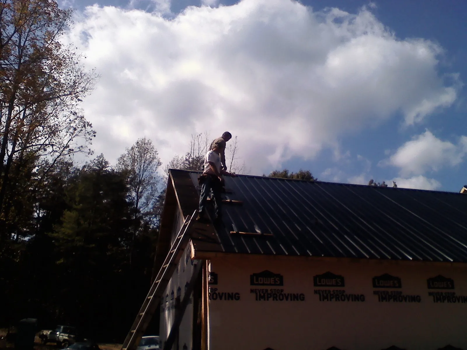 Roofer fastening dark metal panels high against a cloudy sky, from a Roof Inspection job in Feura Bush