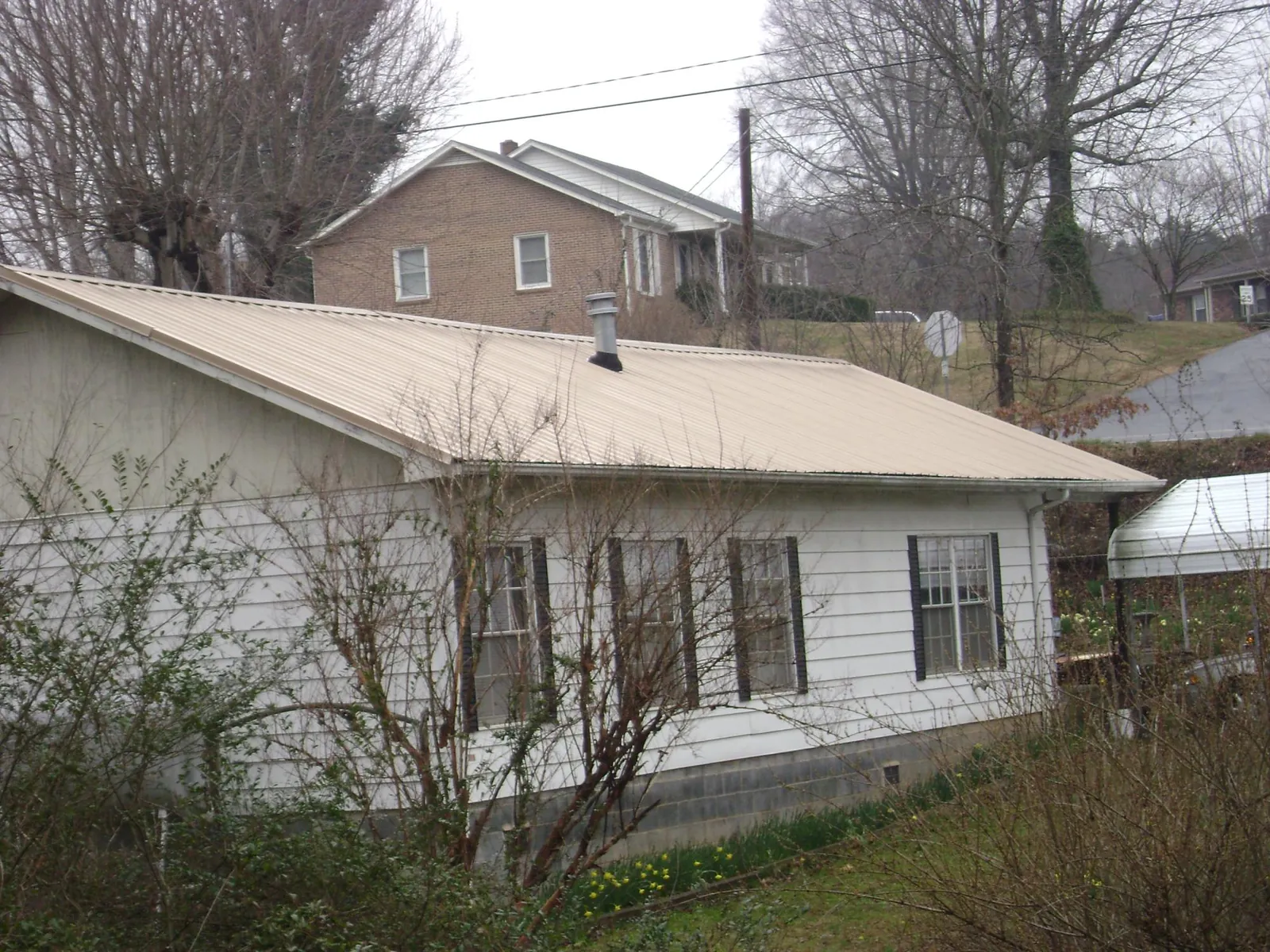 Tan metal roof on a white sided house set into a hillside — Commercial Roofing by Roofing Brothers in Feura Bush